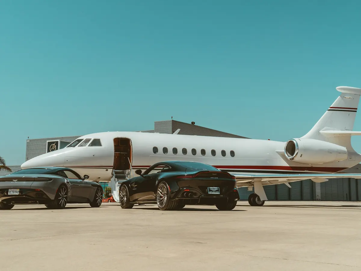 A business jet with its door open beside cars on a sunny ramp